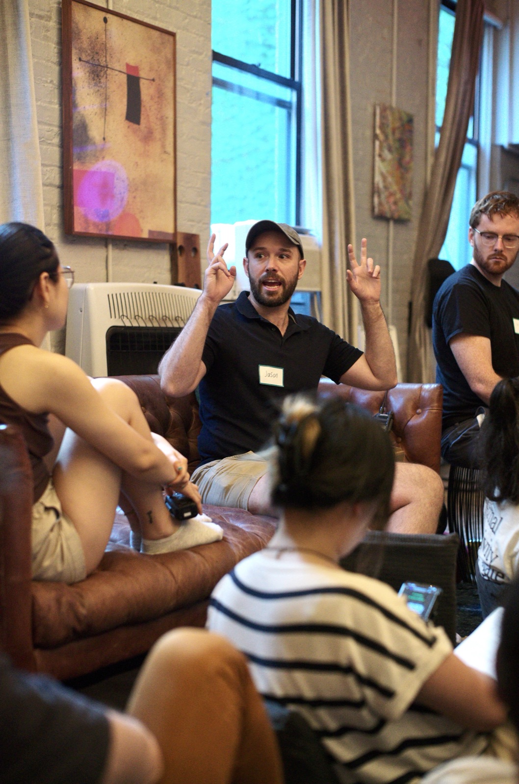 An attendee gestures mid-explanation in the circle of leather couches during the indoor session.