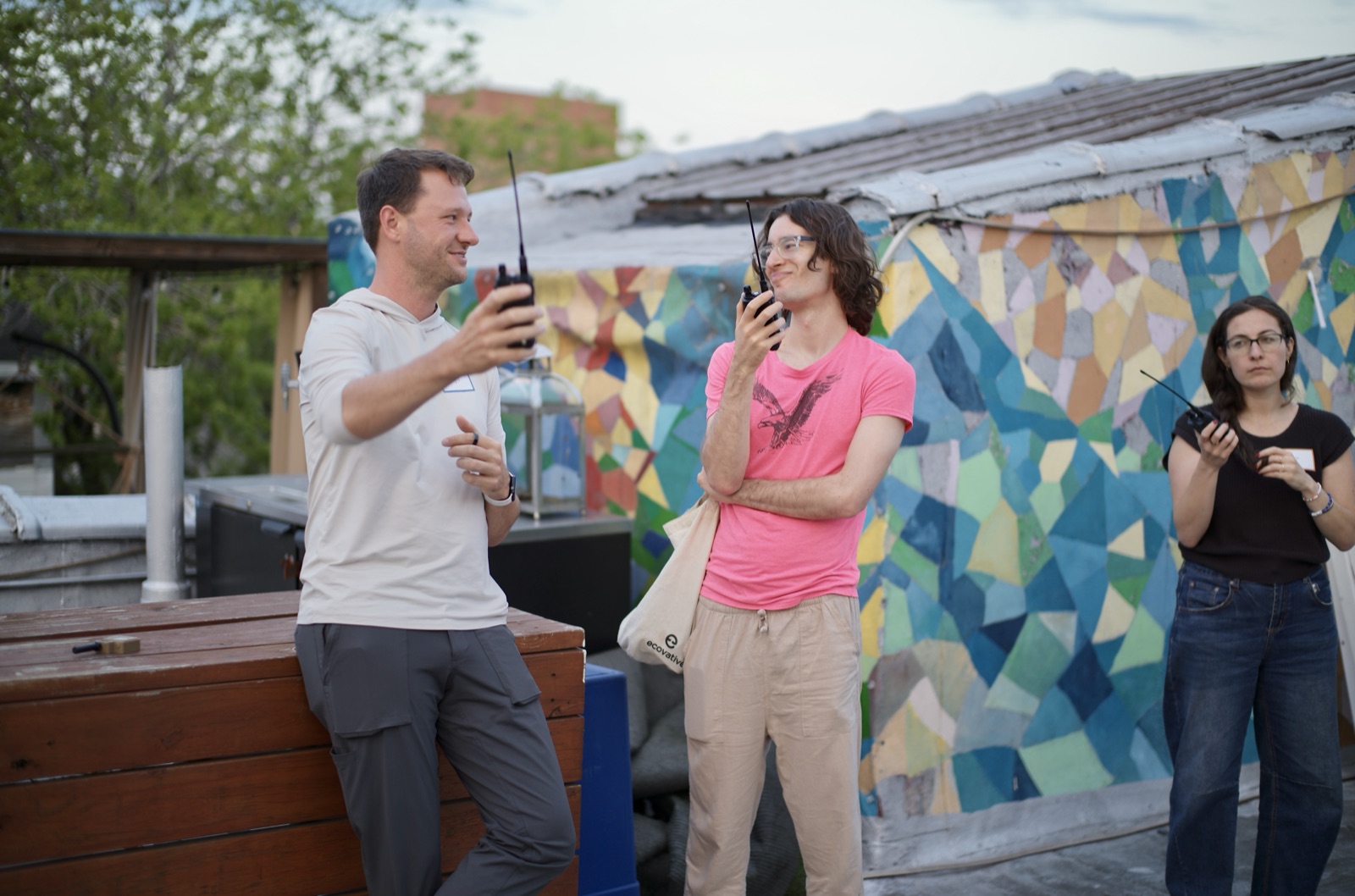 On the rooftop afterward, attendees test FRS handheld radios against a painted geometric mural in the evening light.
