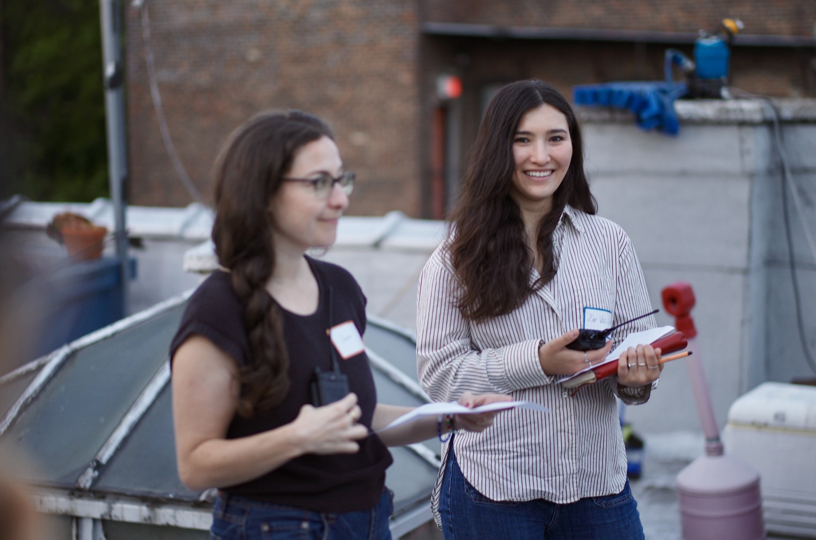 Two attendees compare radios and notes on the rooftop as the light fades over Brooklyn.