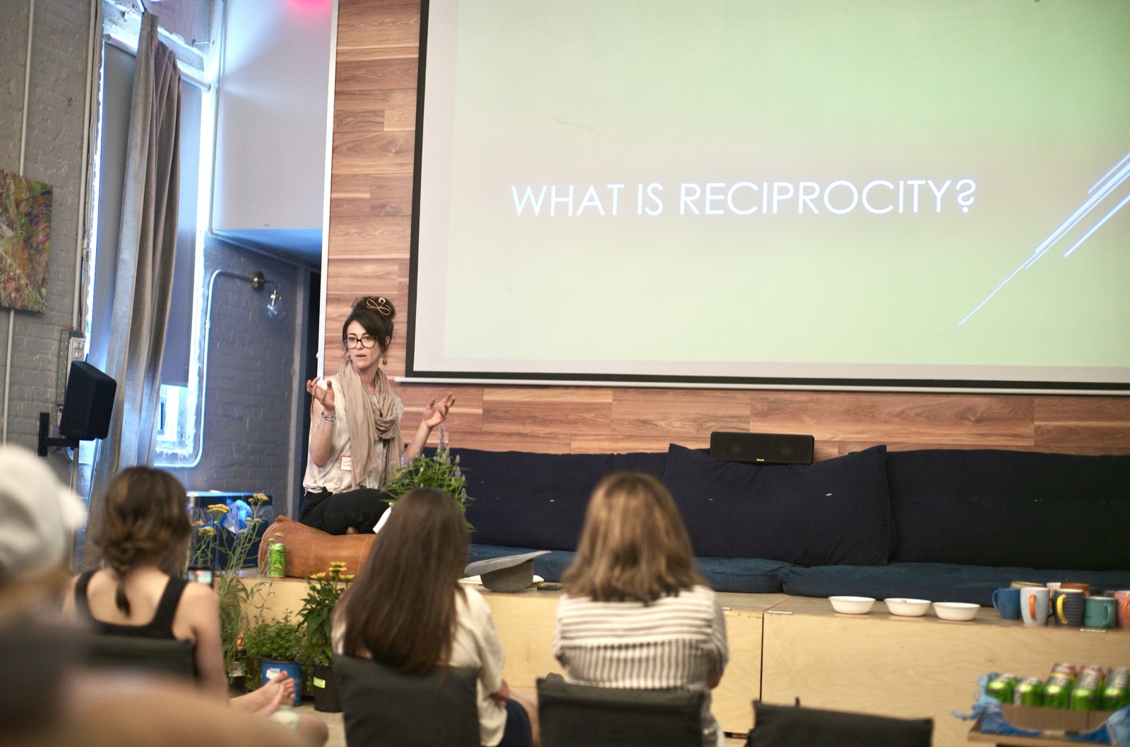 Lauren Sadowsky, the horticulturist leading the lab, opens in front of a projected "What is reciprocity?" slide, potted herbs beside her and the room seated on floor cushions.