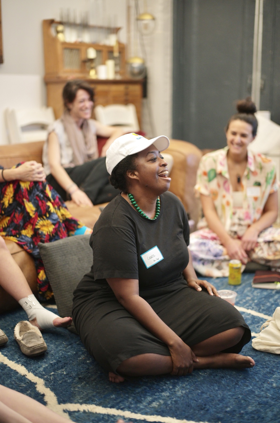An attendee in a white cap laughs during the opening circle, seated on the blue rug.
