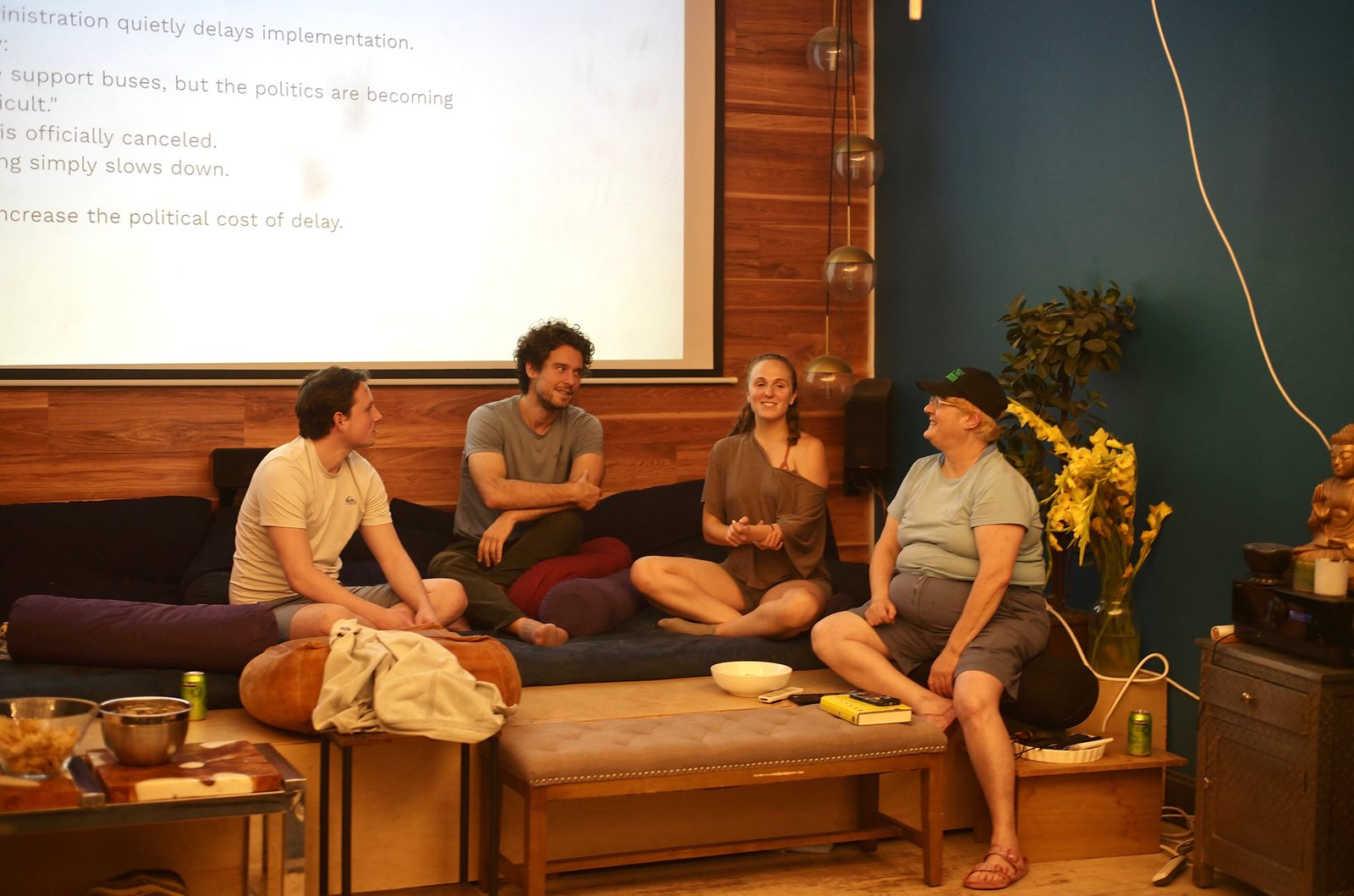 A breakout group works the mayor-gets-cold-feet scenario from the daybed, the prompt projected overhead: nothing is officially canceled, everything simply slows down.