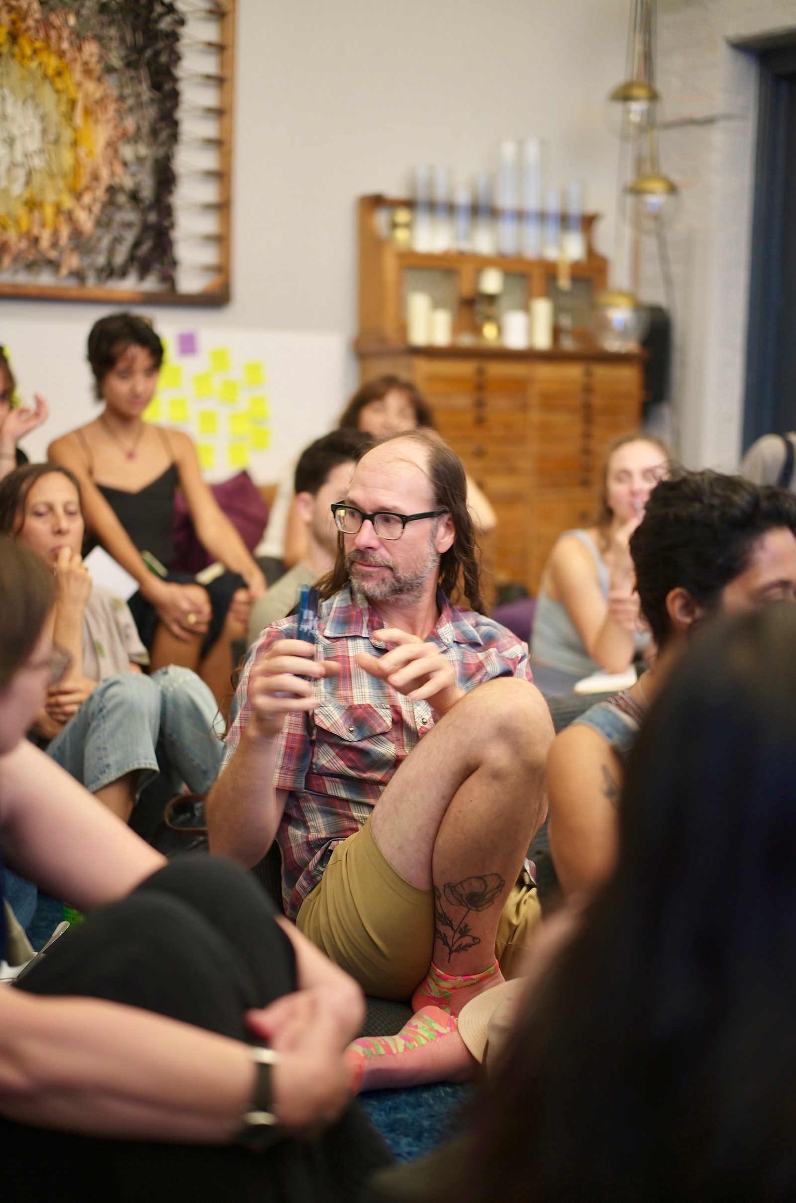 A participant makes a point to the circle, glass in hand, the room turned toward him.