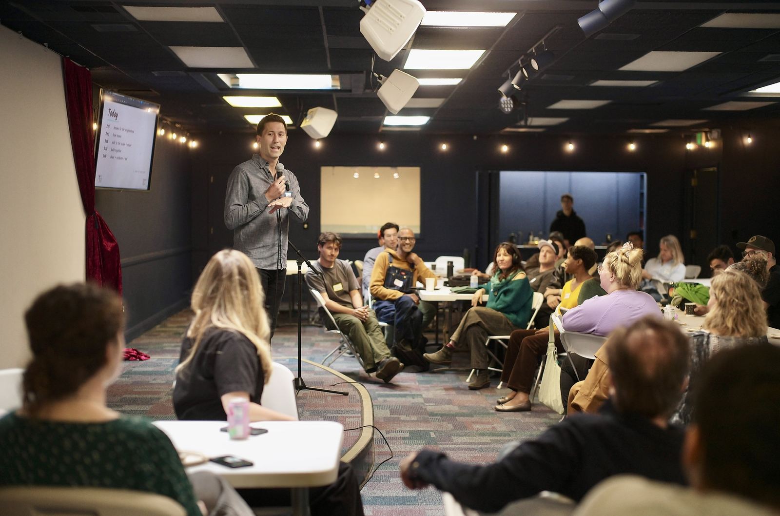 A full room for dream sharing: Josh Nesbit at the mic, the run of show on the screen, neighbors at tables