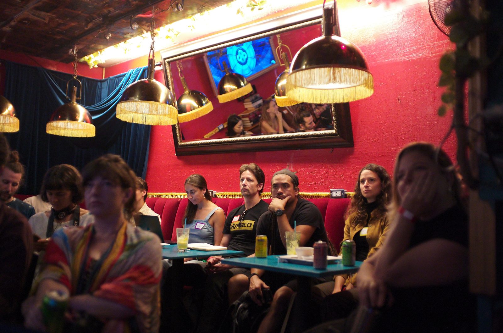 The front booths under the fringed brass lamps, notebooks and seltzers on the tables, a slide reflected in the mirror above.