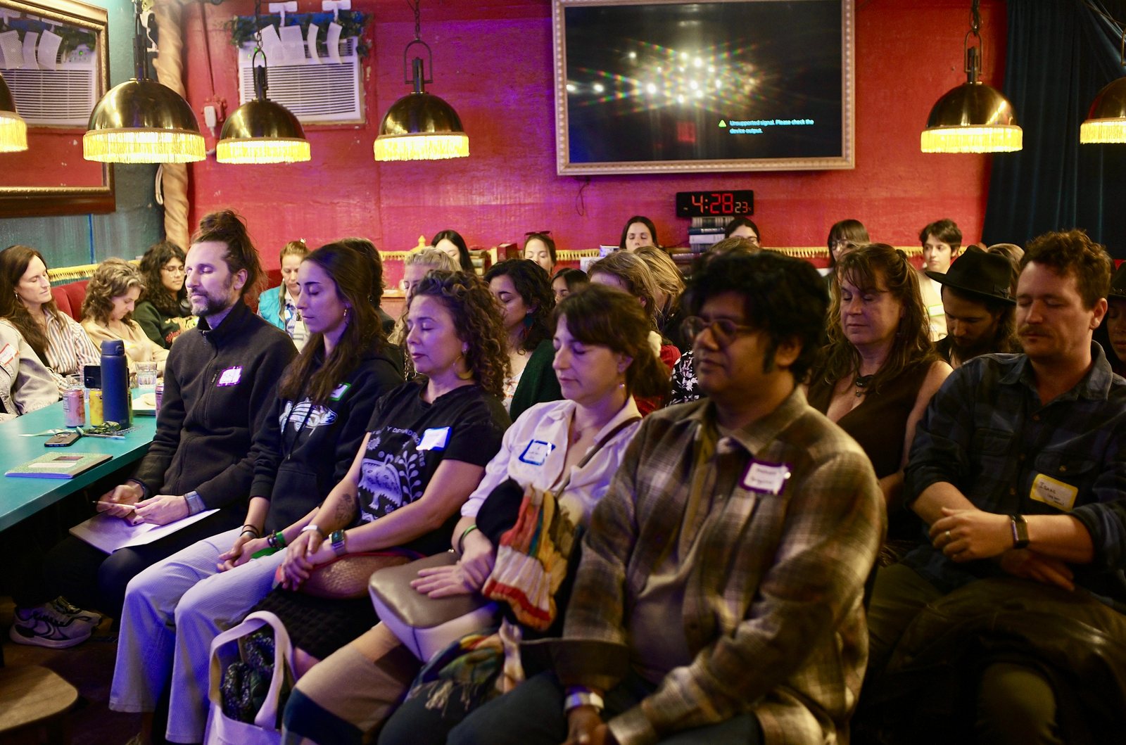 The front row with eyes closed during the whale listening journey, name tags on, the room full behind them under the brass lamps.