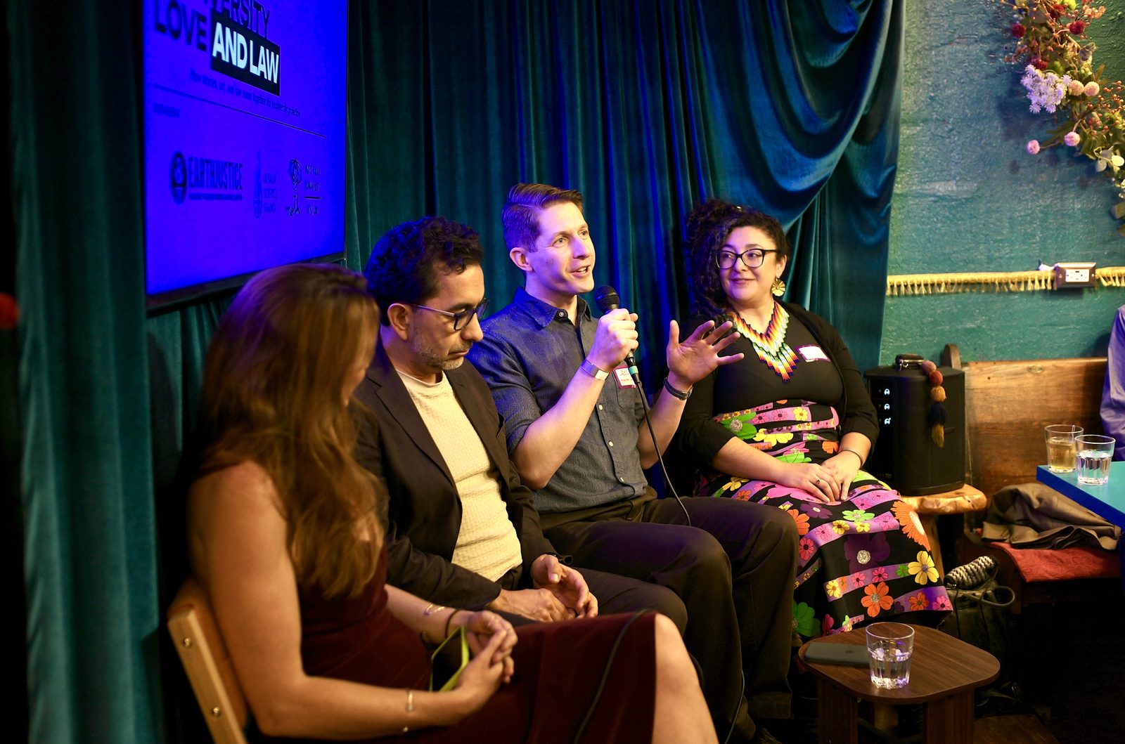 Ben Levitan answering with the microphone, César Rodríguez-Garavito and Roxi Shohadaee beside him under the flowers.