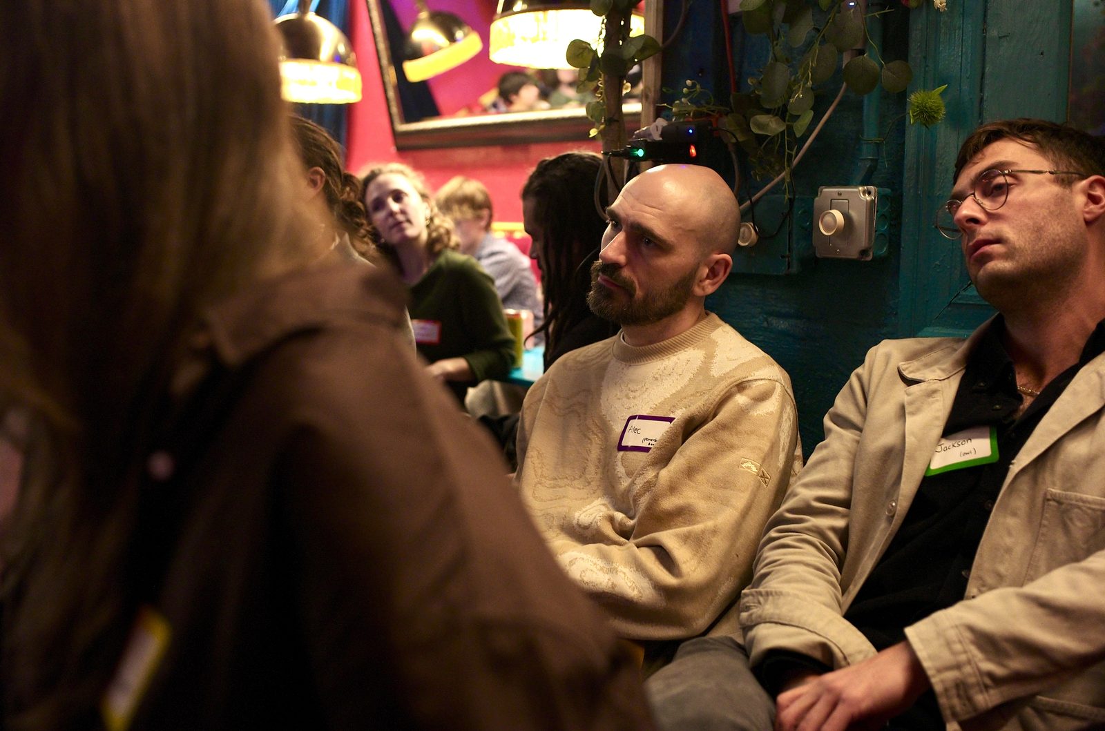 Two listeners in the middle of the room following the conversation, one looking over his glasses.