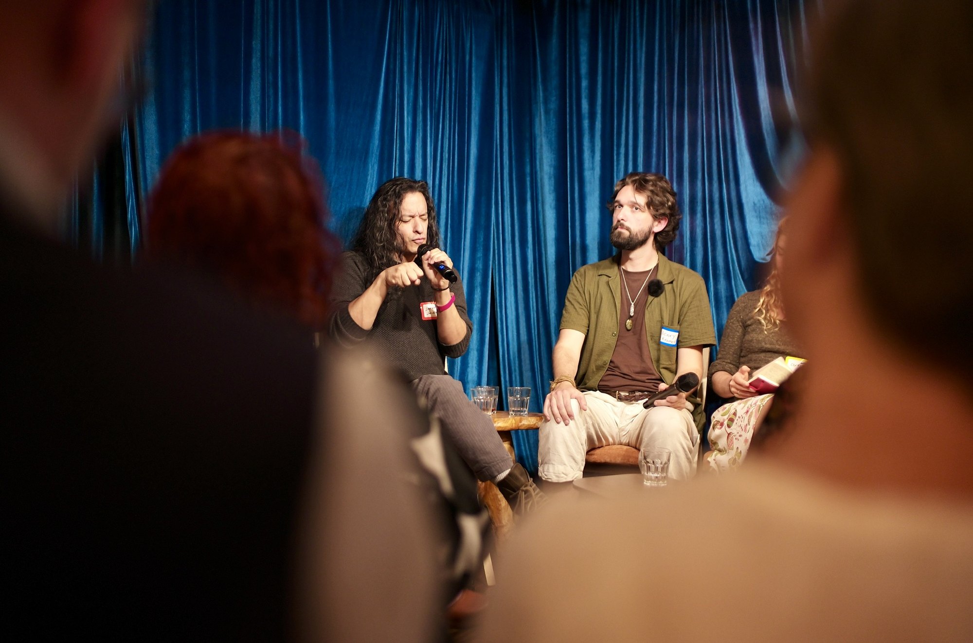Jeremy D Johnson answers into the microphone, Henry Kramer listening beside him against the blue curtain.
