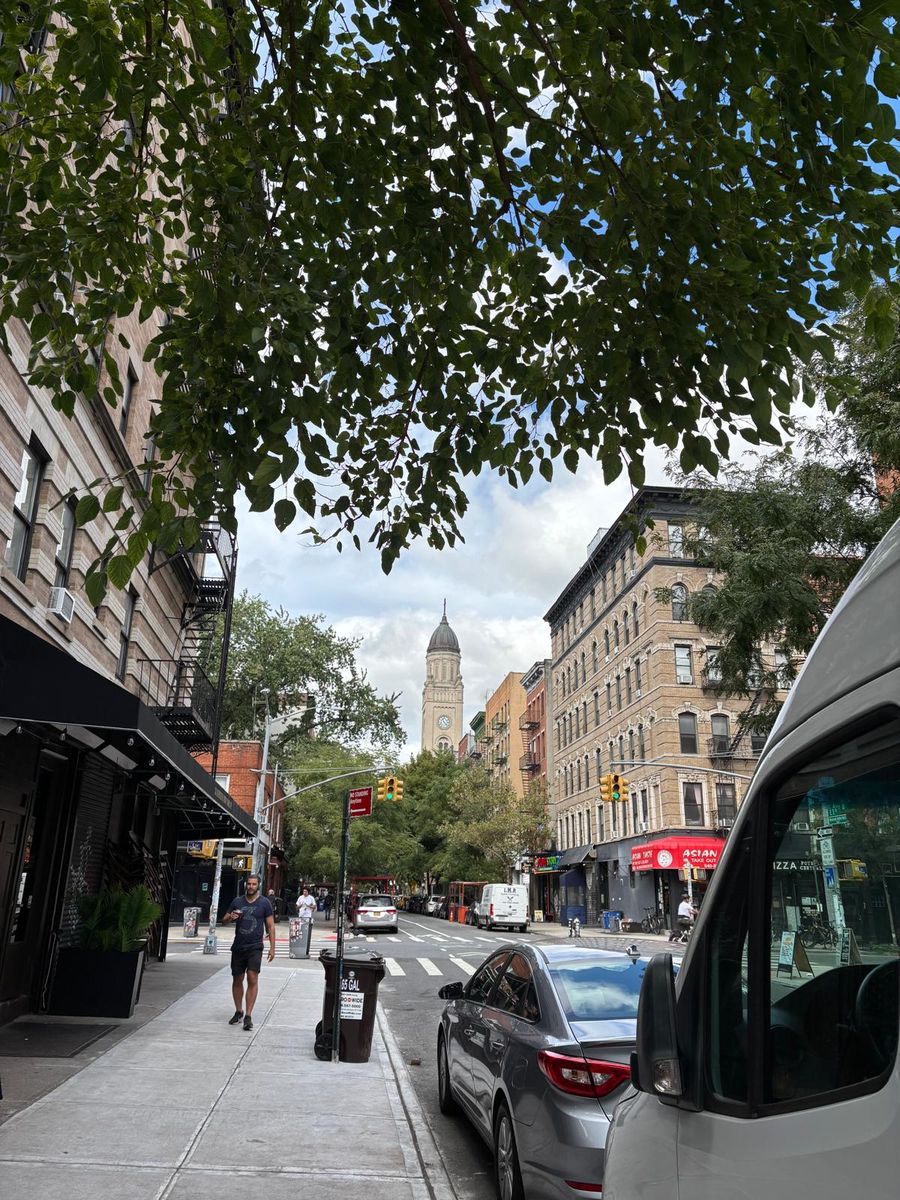 Looking up a tree-lined East Village block on the way east, a church tower at the far end.