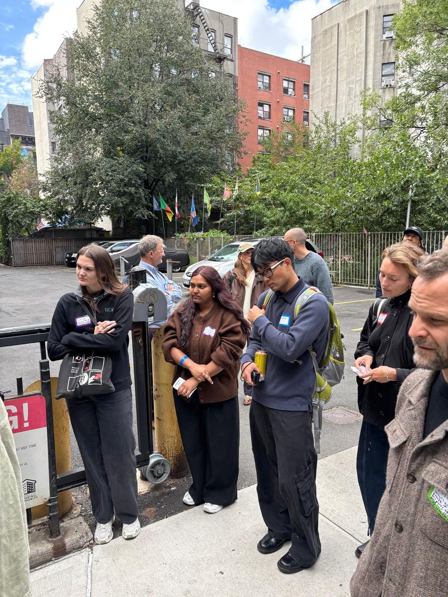 Walkers listening on the sidewalk beside a fenced lot.