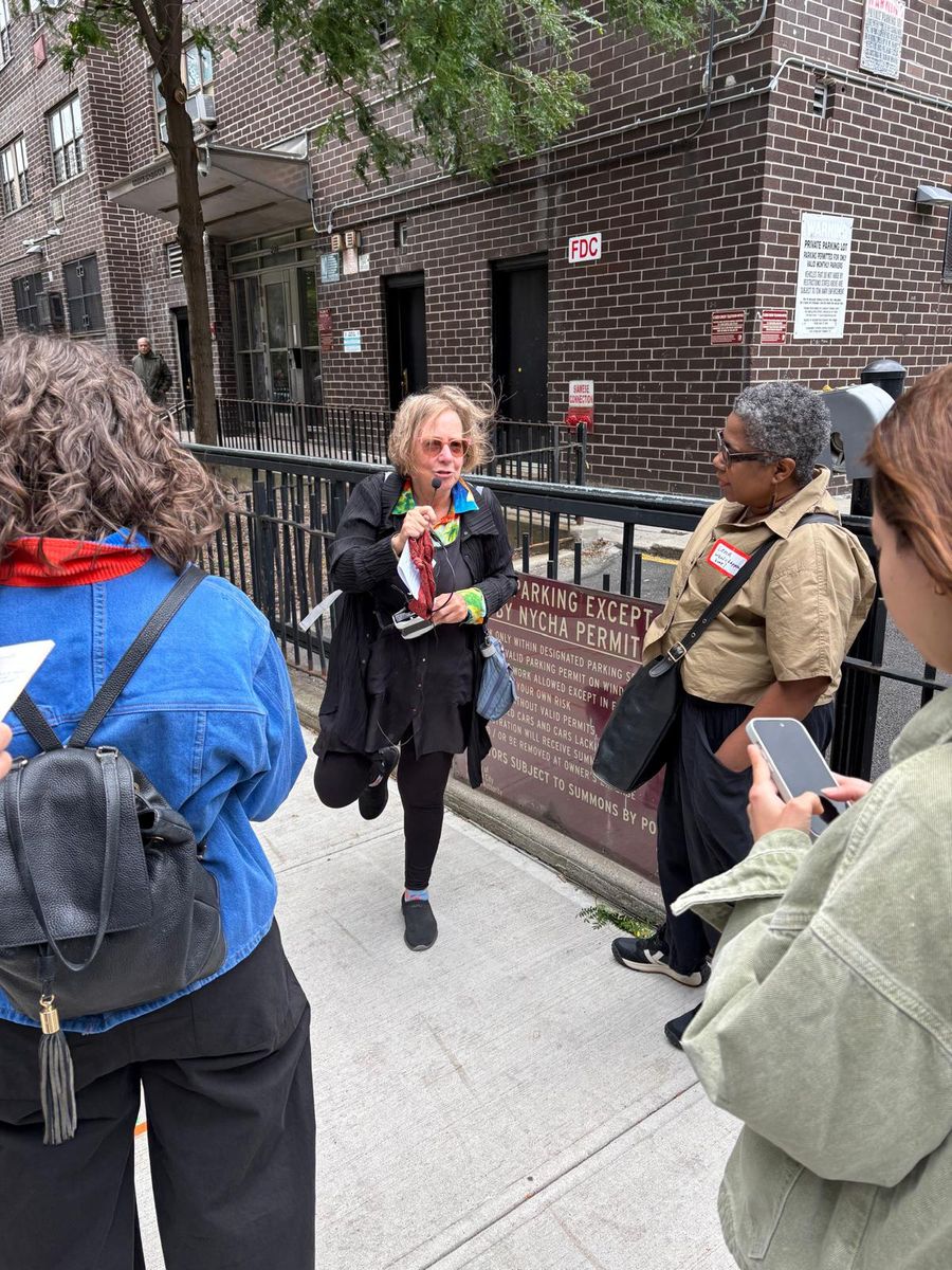 Wendy Brawer speaking at a railing by the brick housing, the group around her.