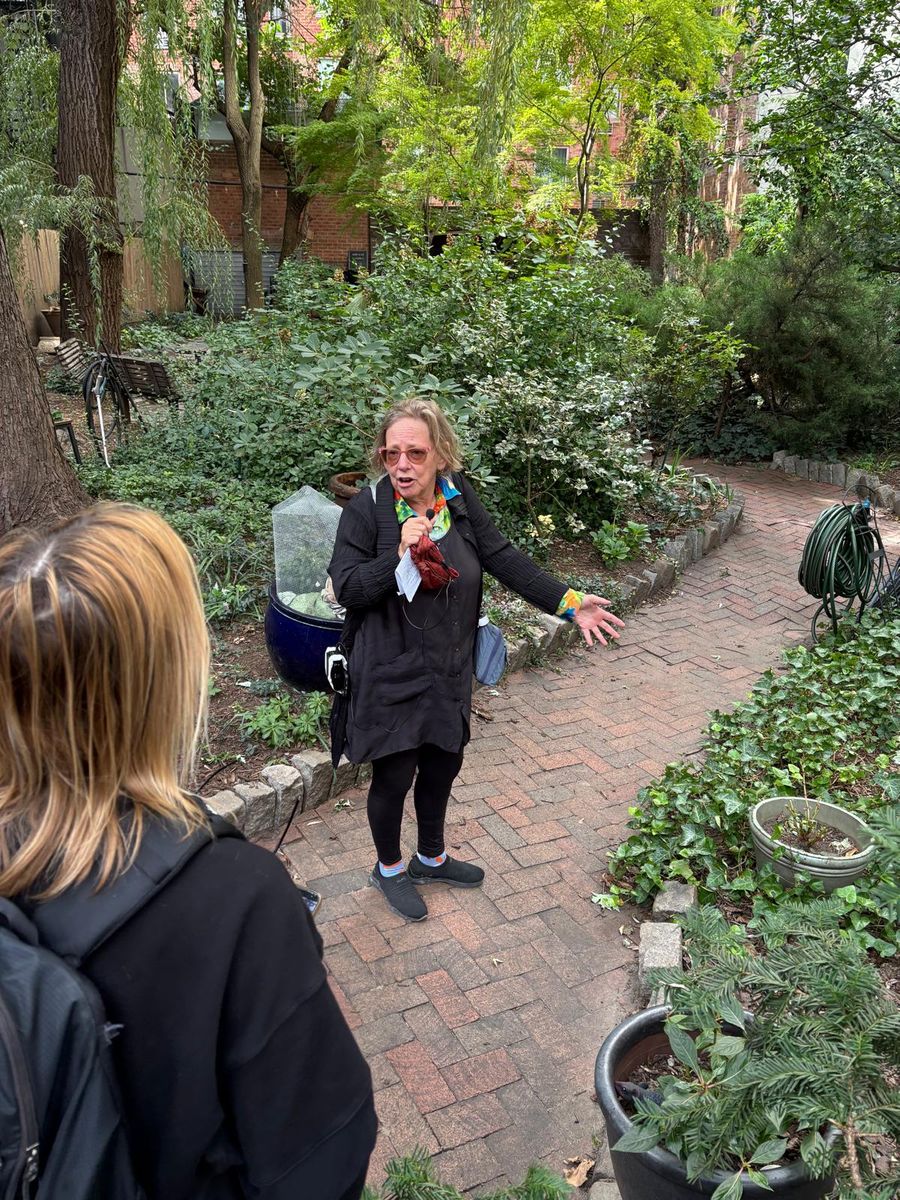Wendy Brawer in the middle of the Miracle Garden, arms open, the group around her among the plants.