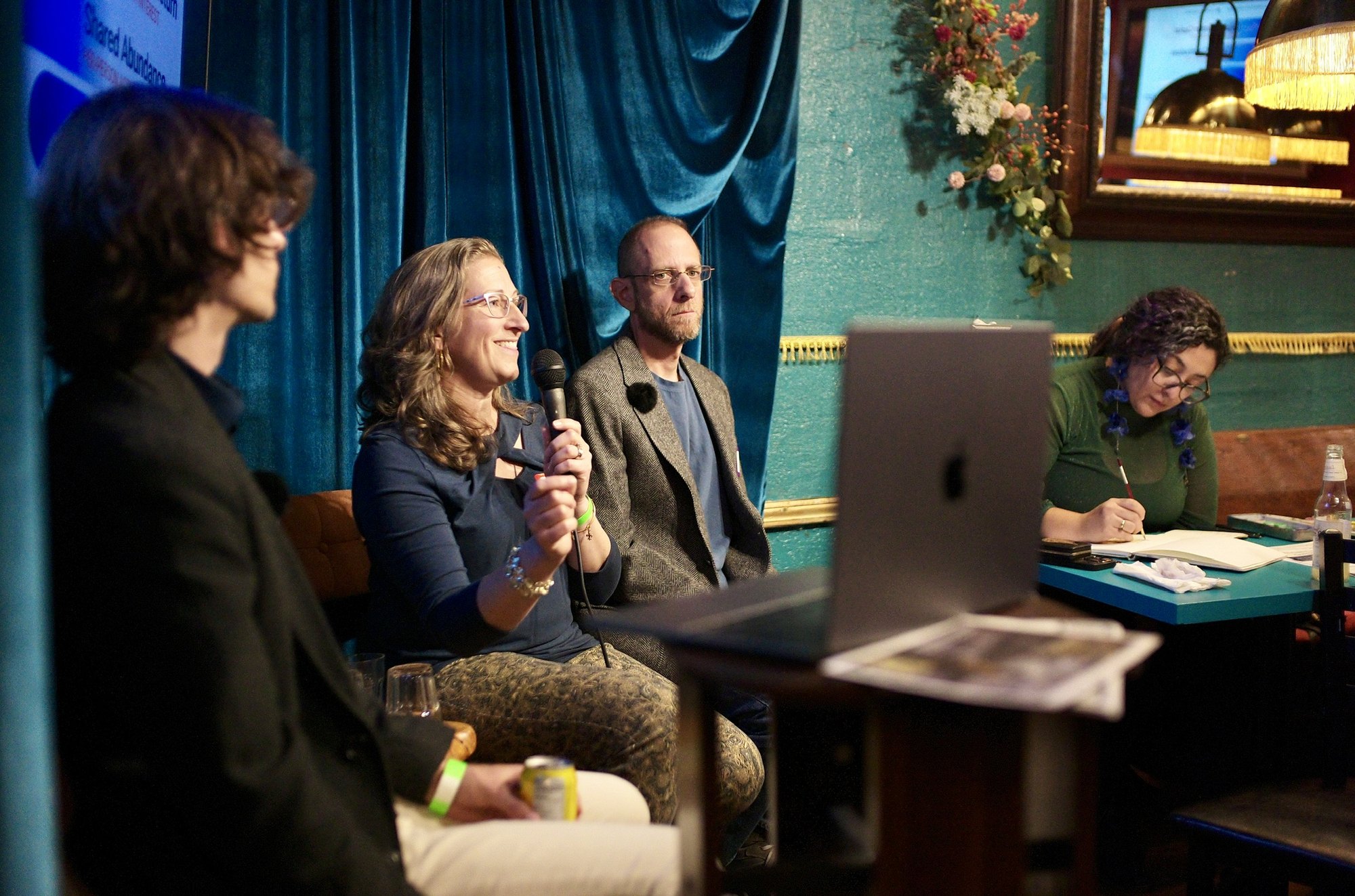 The Collaborative Operating Agreement: a speaker at the microphone between the other two builders, the laptop open on the stand.