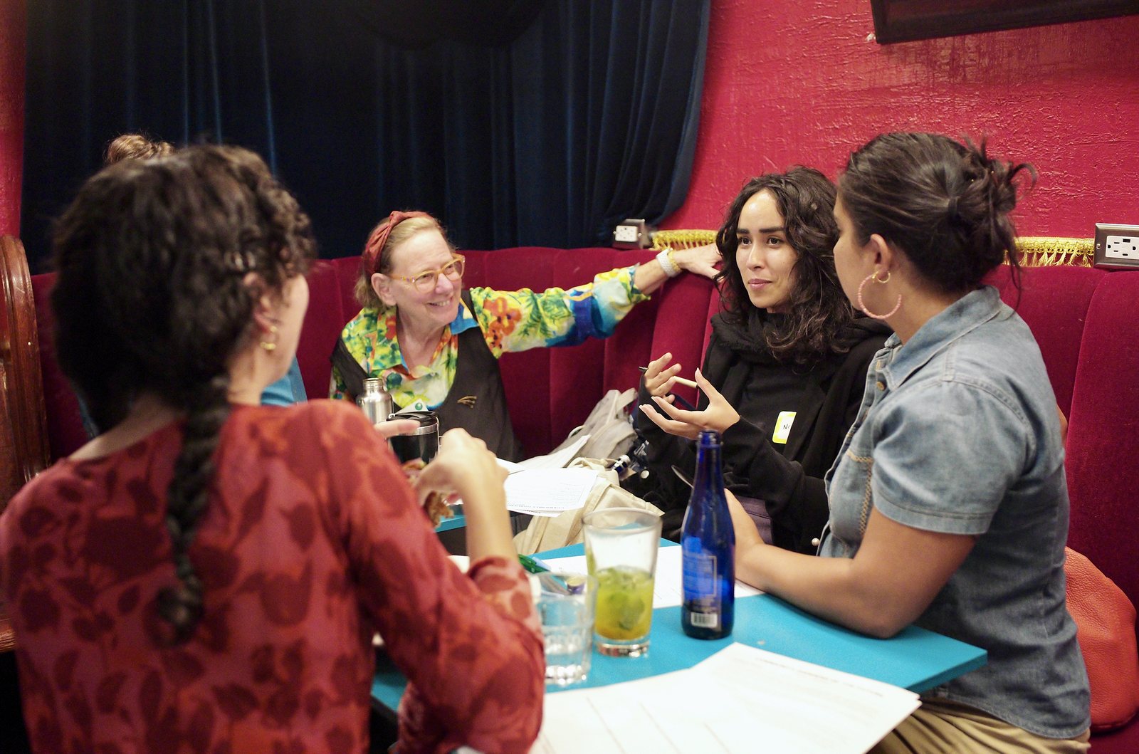 A table in close conversation, one person in a bright floral jacket leaning in with her arm across the banquette.