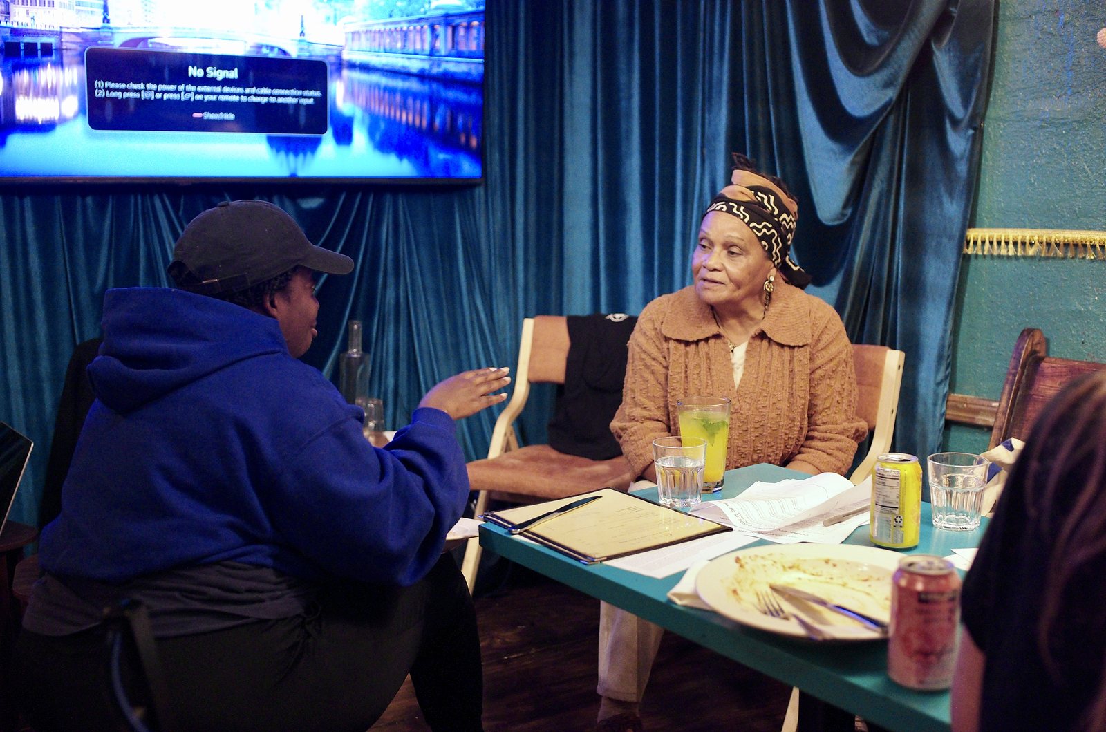 Ena McPherson in conversation with a participant in a blue hoodie at a table beside the stage.