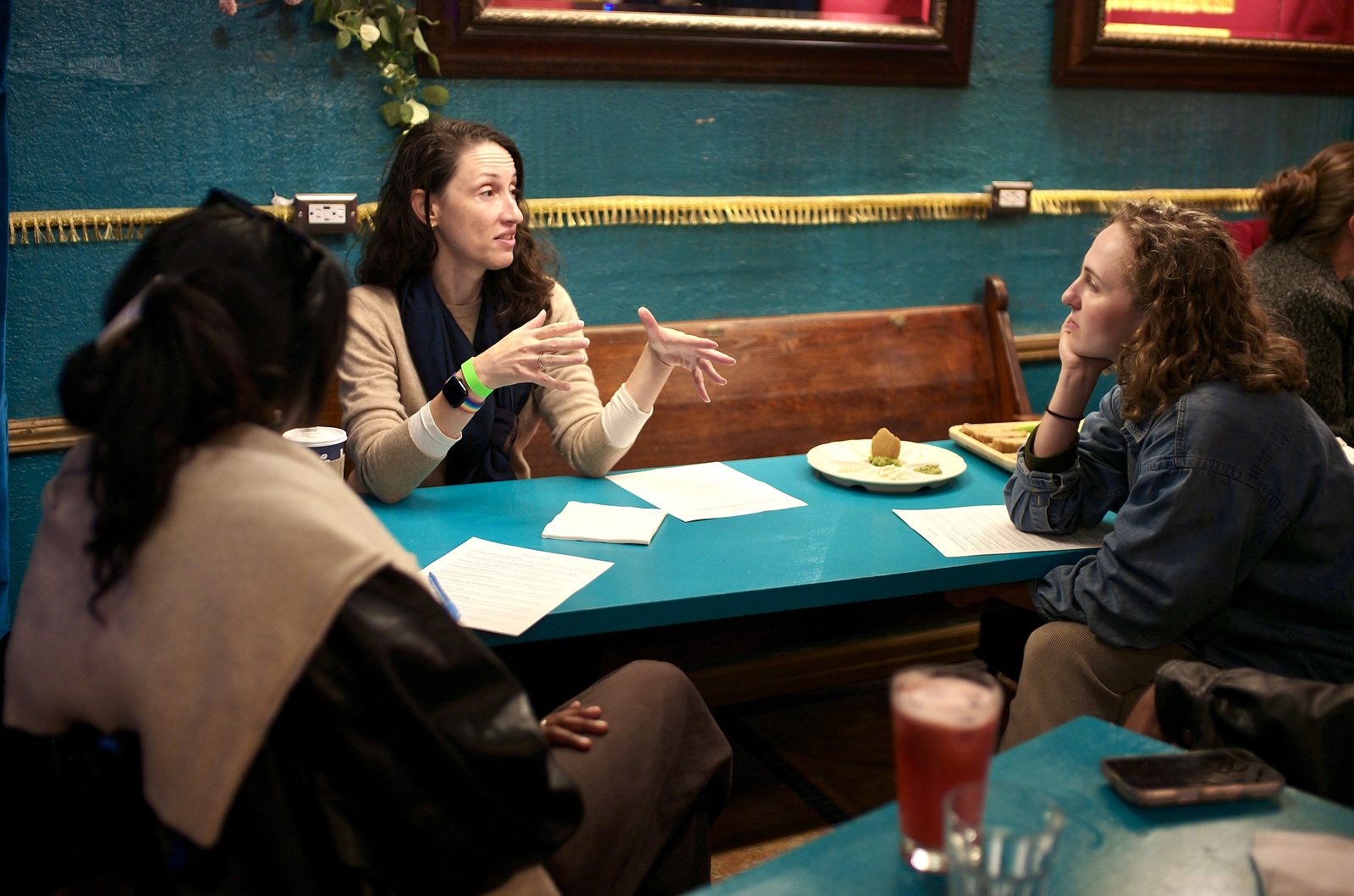 A working group at the blue table, one member explaining with both hands, the handouts spread in front of them.