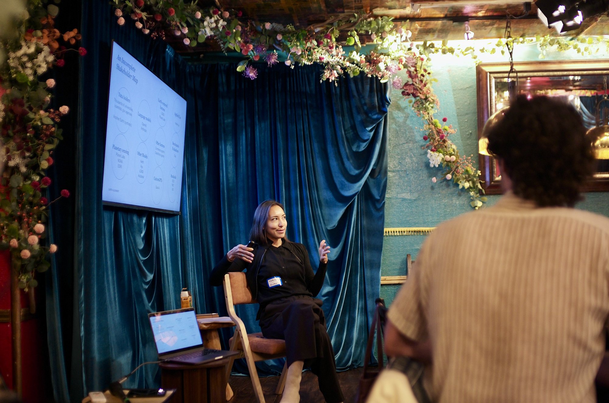 Natalia Vasquez mid-talk, the room seated on every surface under the string lights.