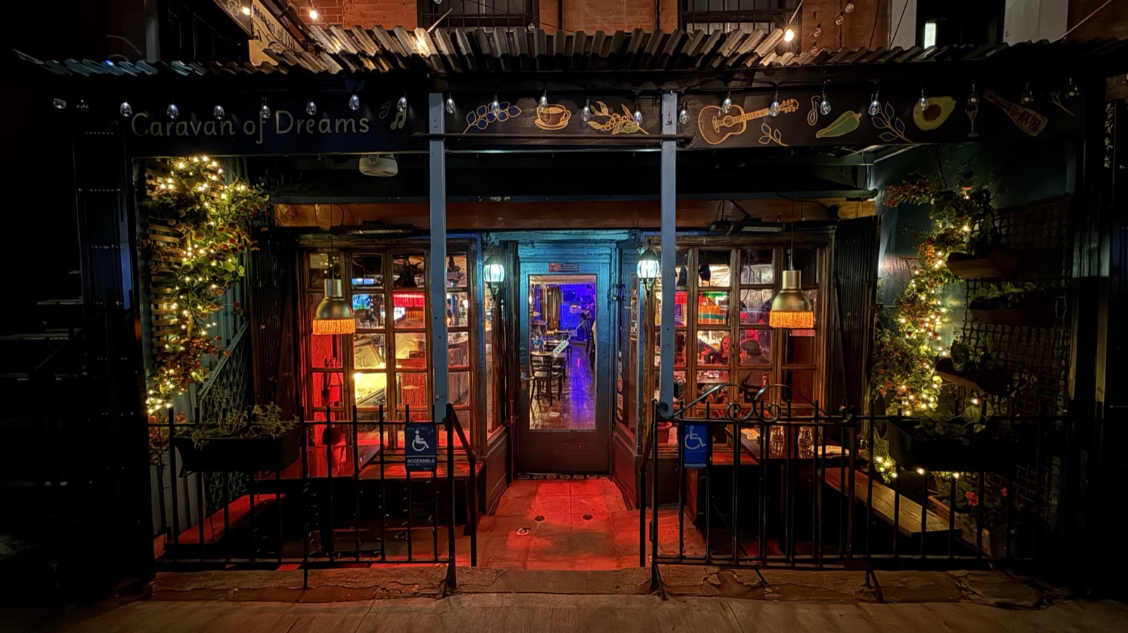 The Caravan of Dreams storefront at night, glowing with string lights, fairy-lit greenery, and diners inside