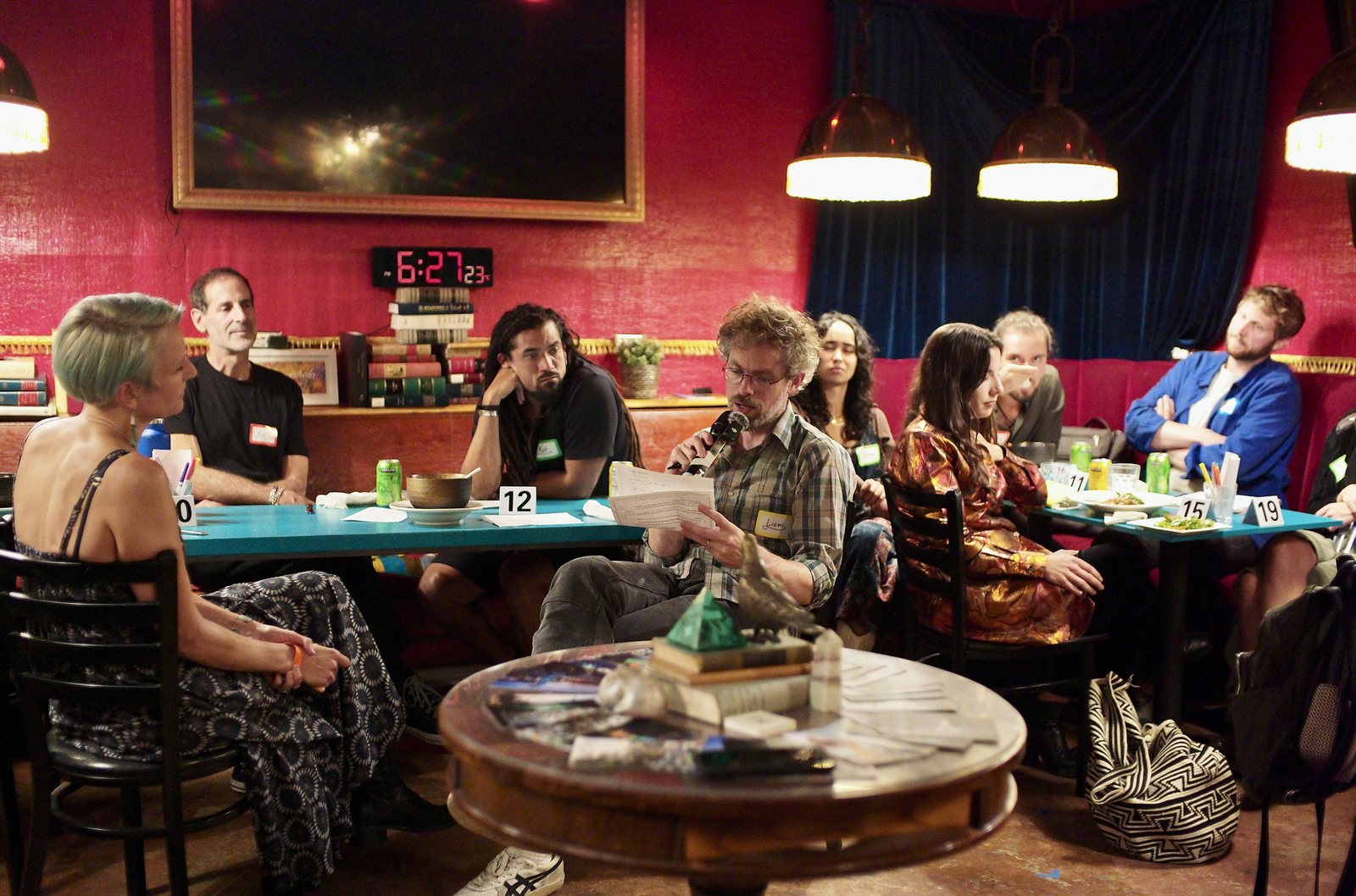 A working dinner: guests at the numbered teal tables, one reading from a card