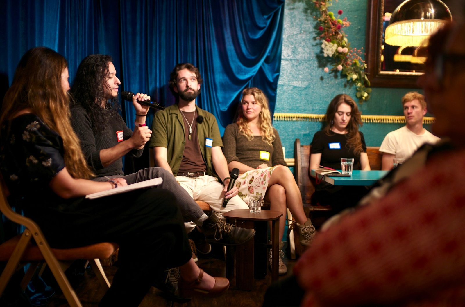 A five-person panel against the blue velvet curtain, one speaker on a wireless mic