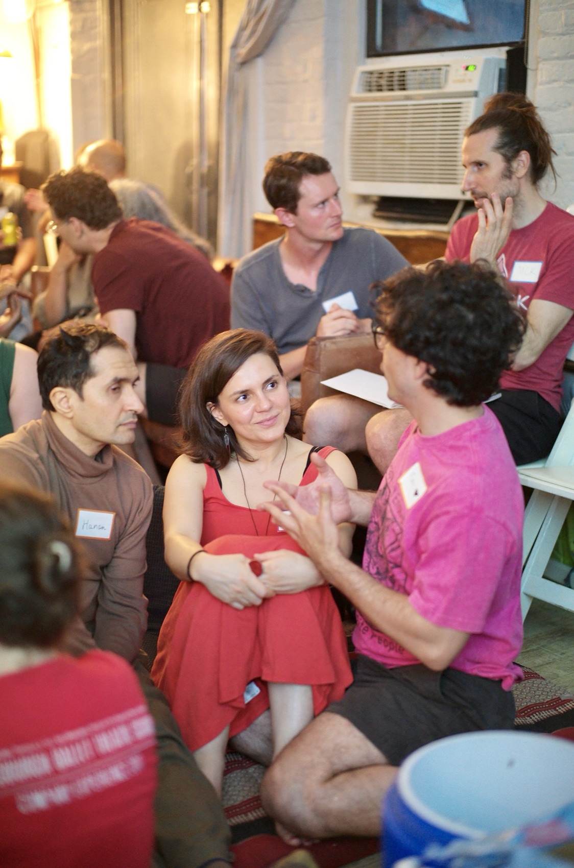 A small breakout group leans in close on floor cushions, mid-conversation during the popcorn round.