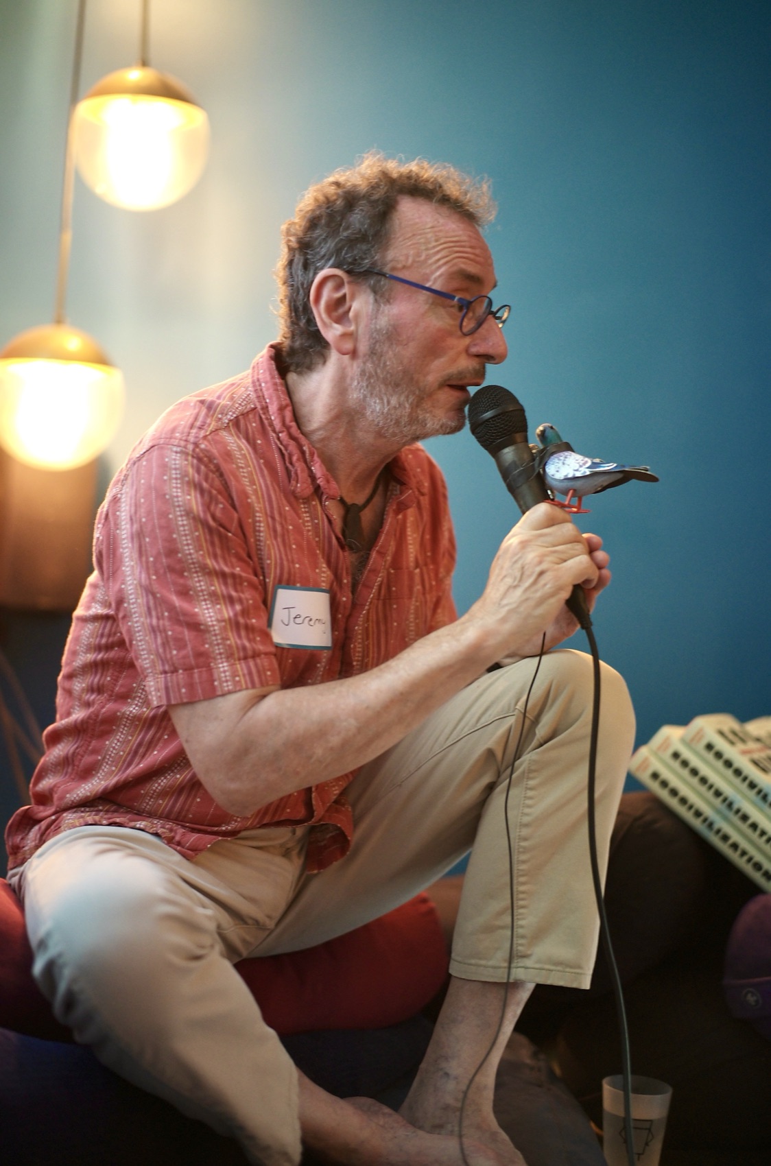 Jeremy Lent speaks into the salon's pigeon-topped microphone, nametag reading 'Jeremy', against the deep-blue wall of Lightning Society.