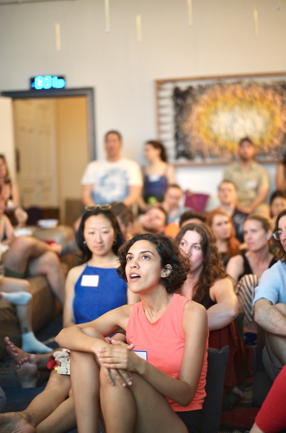 An attendee in a coral top listens intently from the front, the full room attentive behind her.