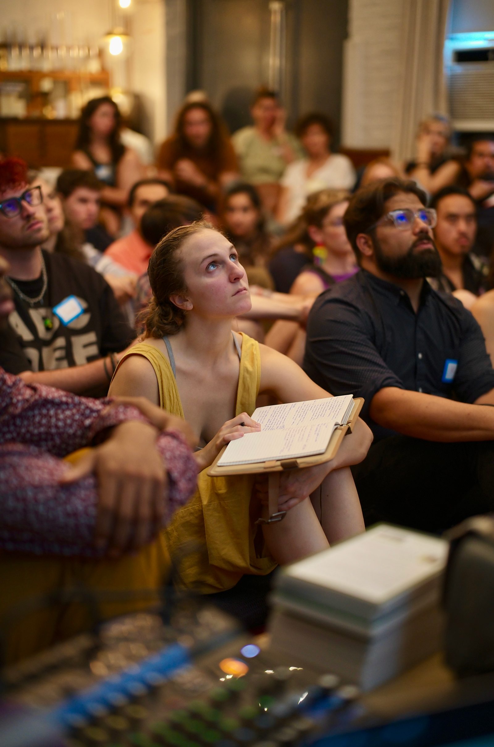 An attendee listening with an open notebook in her lap, head tilted up toward the speaker.