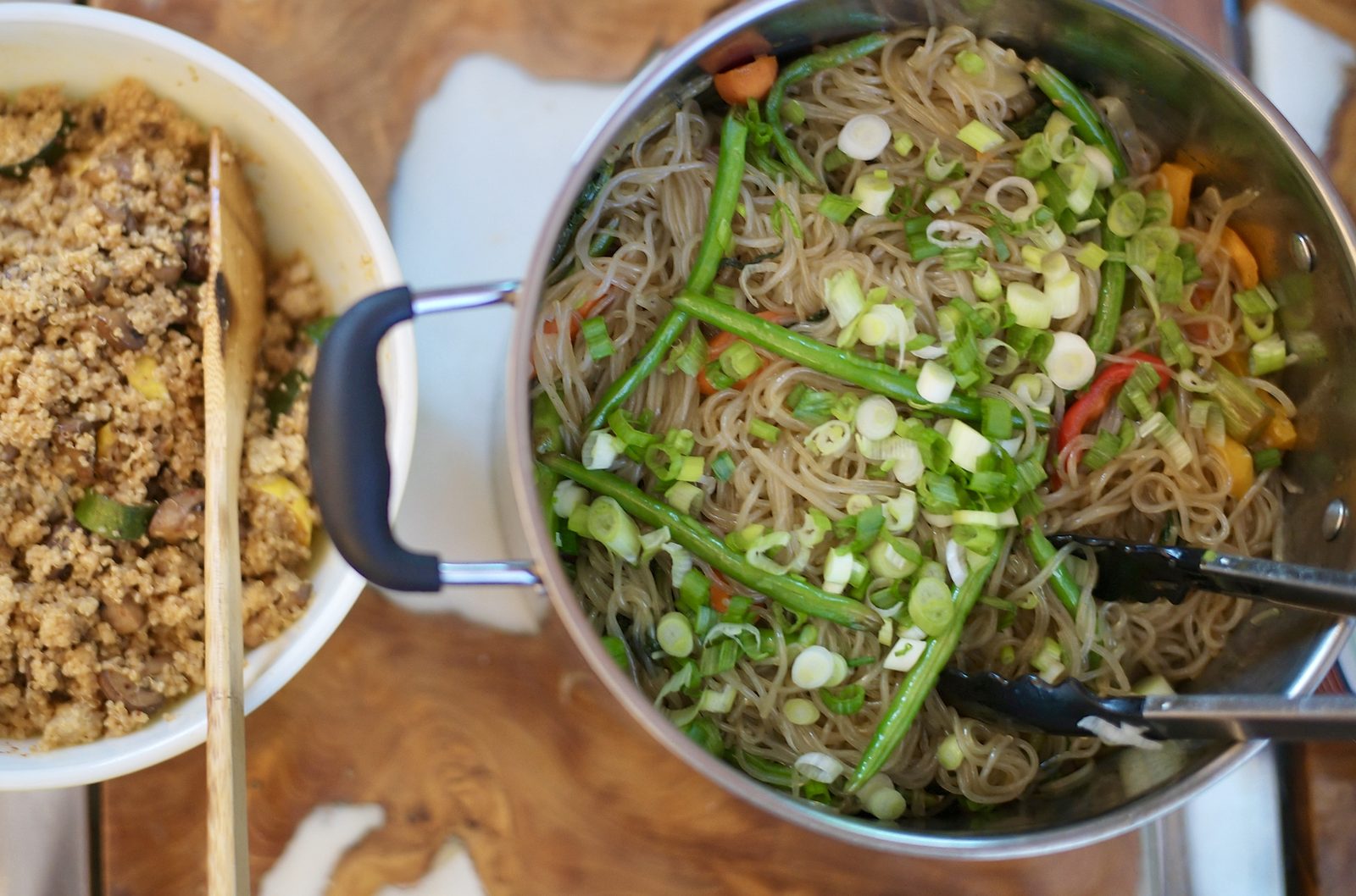 The chefs' work from above: a pot of noodles with scallions and peppers next to a tray of grain salad.